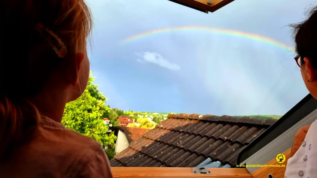 Kleinkind und Mama beobachten Regenbogen aus dem Dachfenster